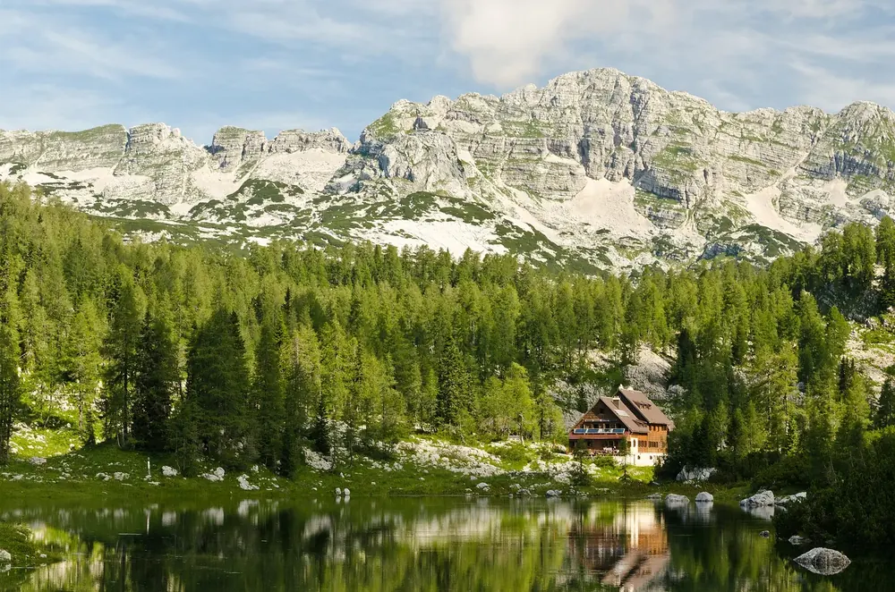 Koča pri Triglavskih jezerih: mountain hut on the shore of a mountain lake, with conifers and pale limestone peaks behind