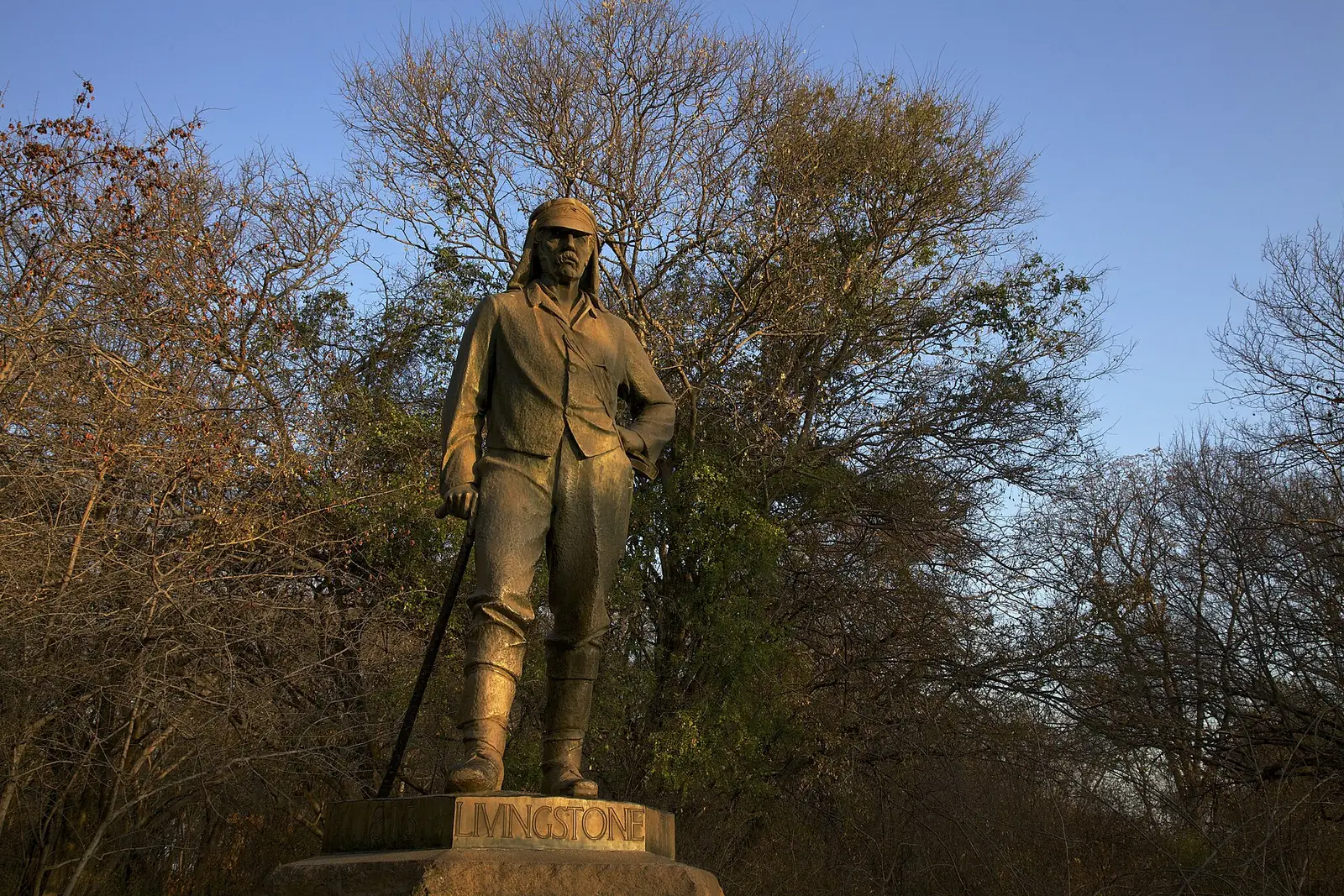 Bronze statue of David Livingstone at Victoria Falls in Zimbabwe, in warm morning light against bare trees