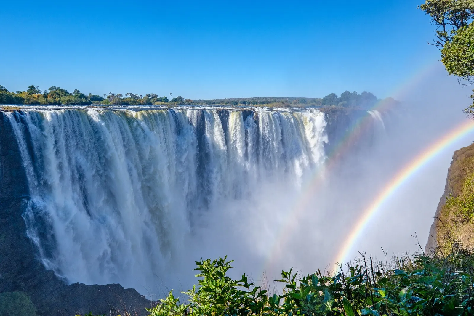 Main Falls of Victoria Falls from the Zimbabwean side: a broad wall of water pouring into the gorge, a double rainbow in the spray