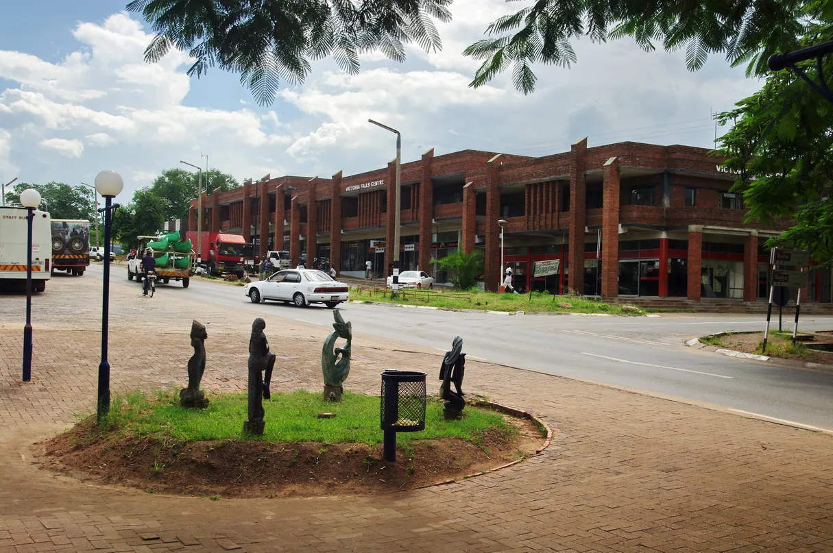 Street in the town of Victoria Falls with wooden sculptures on a traffic island and a red-brick shopping block