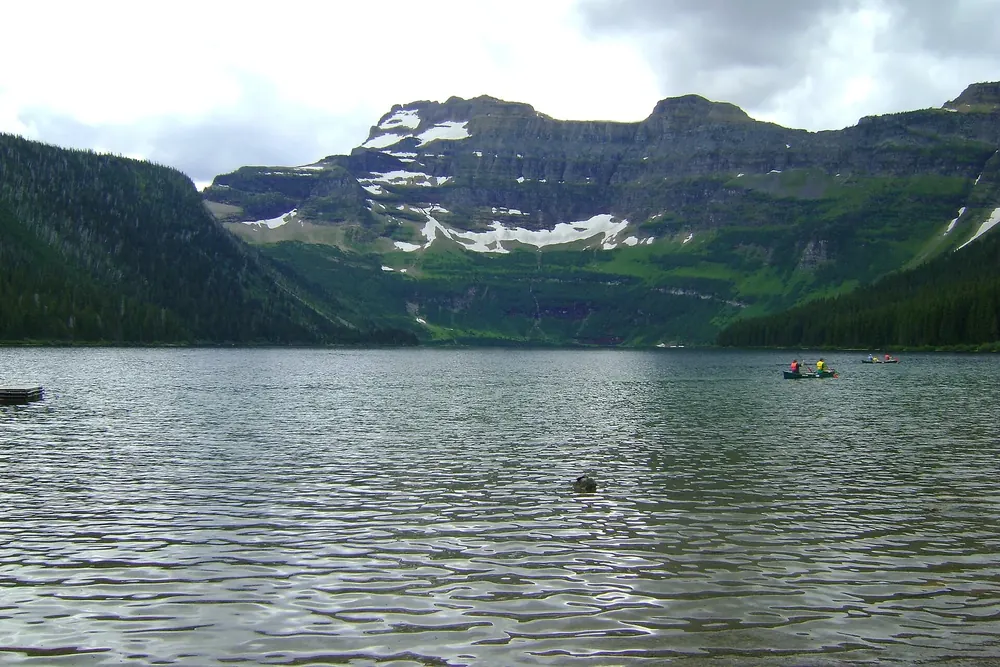 View south across Cameron Lake in Waterton Lakes National Park to rock walls and snowfields, small canoes on the lake