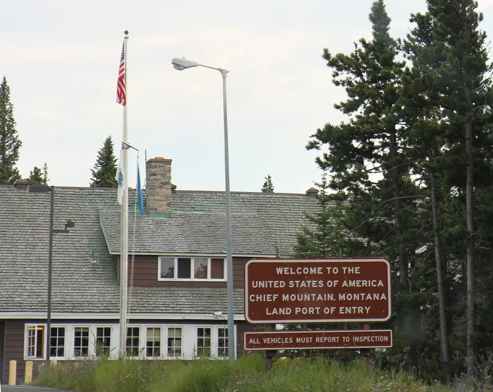 Chief Mountain border station in Waterton Lakes National Park: wooden building with a welcome sign and flagpoles among tall conifers