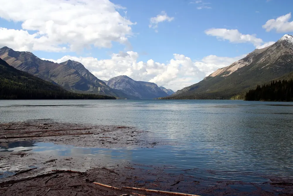 Upper Waterton Lake in Waterton Lakes National Park: wide mountain lake between steep, forested slopes, flat rock slabs on the shore in front