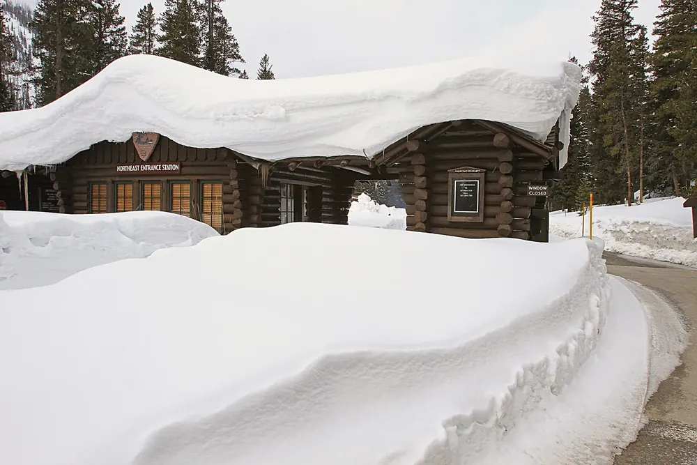 Yellowstone National Park's Northeast Entrance in April: log-cabin entrance station with metre-high snow on the roof and along the road.