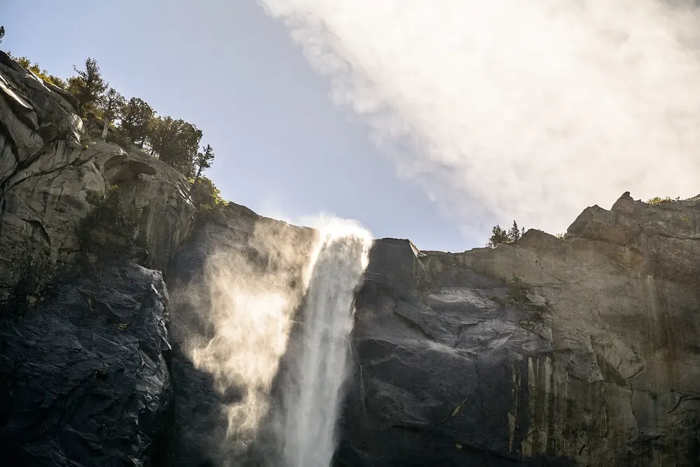 Bridalveil Fall in Yosemite National Park: the waterfall plunges over a dark granite edge, its spray glowing against a bright sky