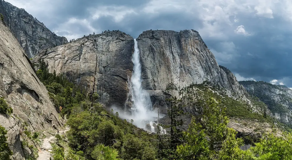 Upper Yosemite Fall in Yosemite National Park from the trail: the waterfall plunges over a huge granite wall, with green slopes in front