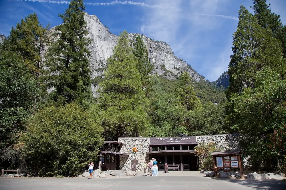 Visitor centre in Yosemite Village: a low building with a wooden canopy between tall conifers and granite walls
