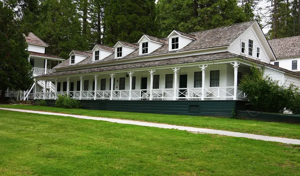 Wawona Hotel: white wooden building with a wraparound veranda and dormers in front of a neat lawn and trees