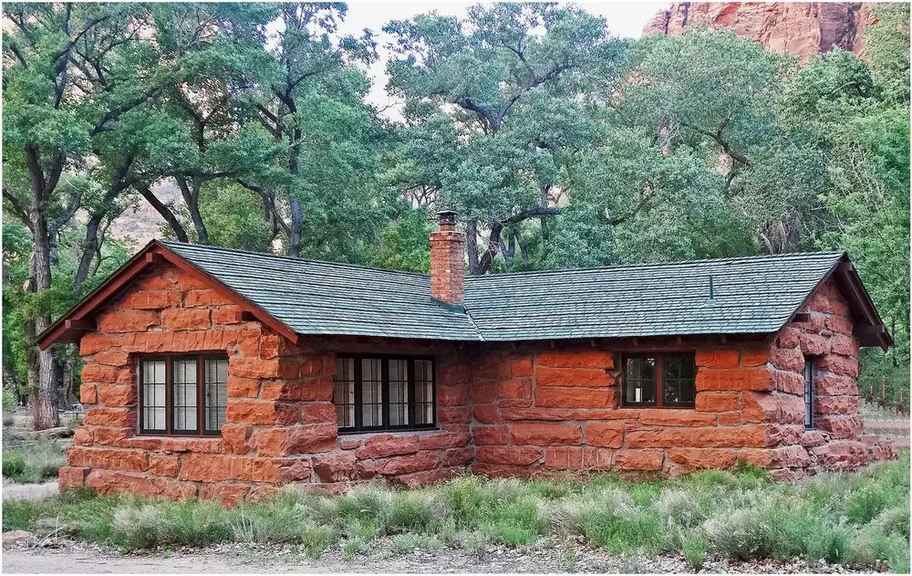 Historic cabin on the Grotto Trail in Zion National Park: a red sandstone building with a green shingle roof among cottonwoods.