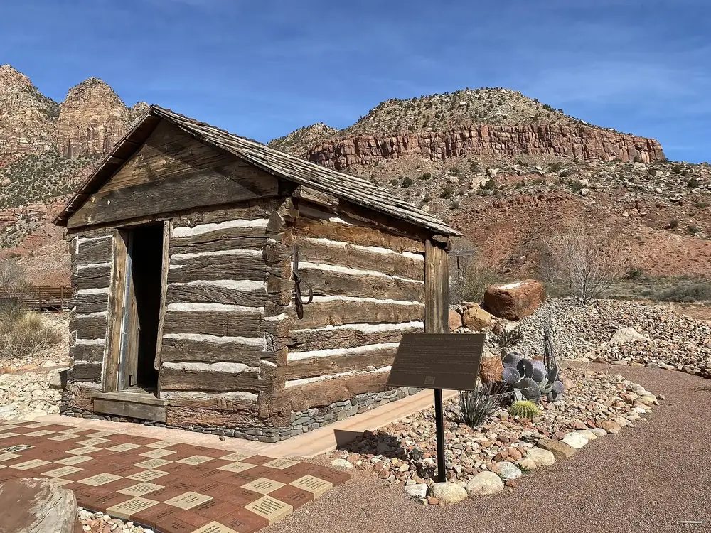 Historic log tithing granary in Springdale, with red rock walls at the entrance to Zion Canyon behind