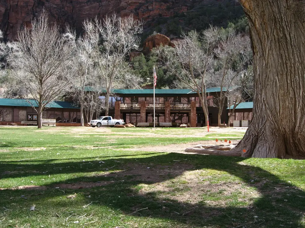 Zion Lodge in Zion National Park: a long main building behind a lawn with tall cottonwoods below red rock walls.