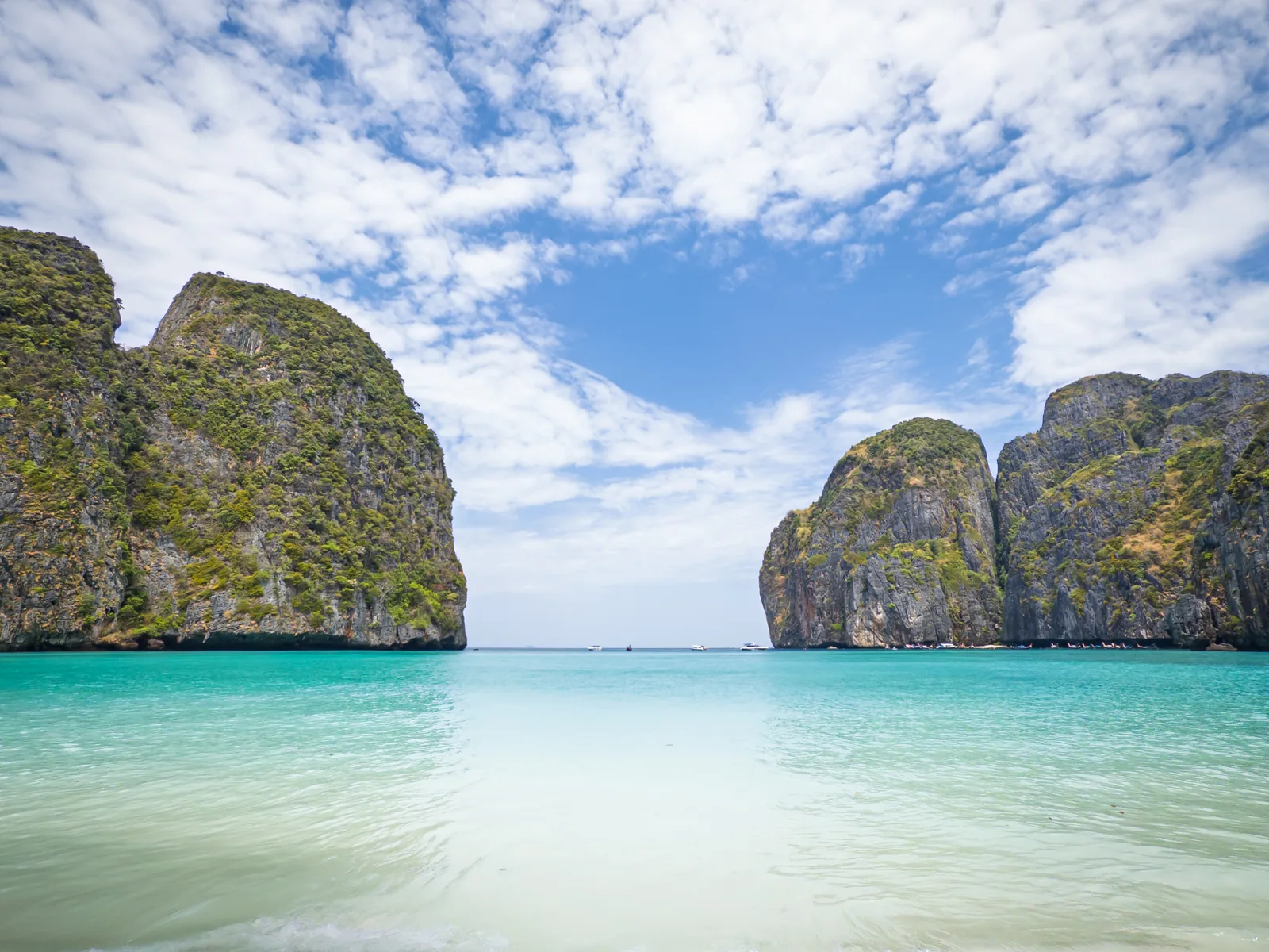 The empty sandy beach of Maya Bay on Ko Phi Phi Le, shallow turquoise water and the limestone cliffs at the bay's entrance on either side