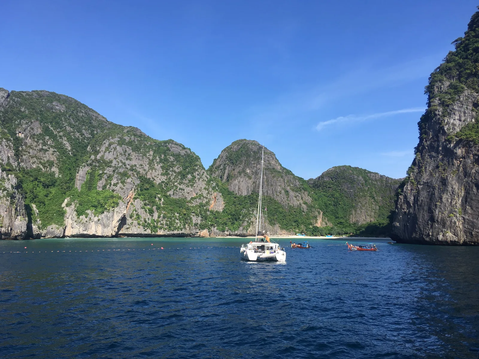 Maya Bay in June 2018, five days after its closure: a catamaran on dark blue water in front of forested limestone hills