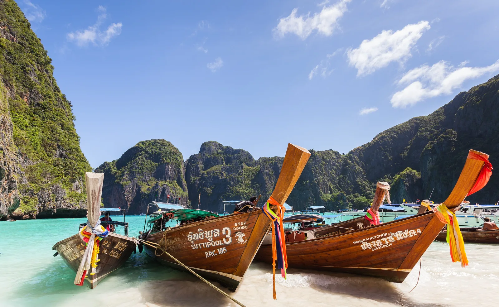Brightly decorated longtail boats on the pale beach of Maya Bay, with the limestone cliffs of the bay behind