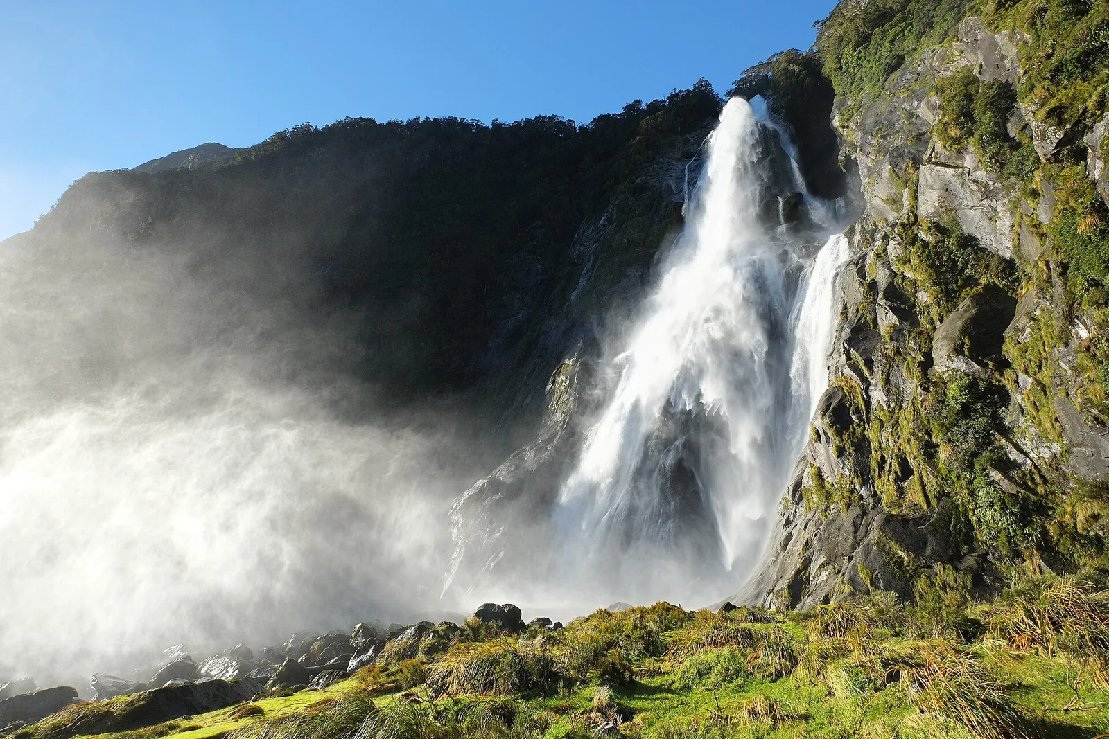 Bowen Falls at Milford Sound pour over a rock edge in the sun, the spray rising as a white cloud