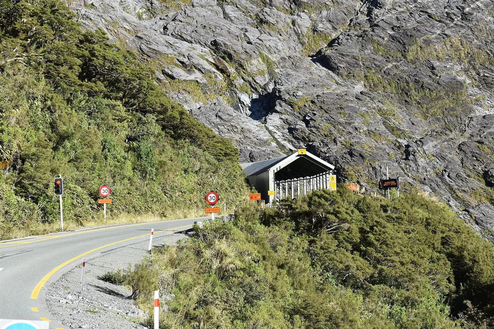 The western portal of the Homer Tunnel on the road to Milford Sound, with traffic lights and a shelter in front of a steep granite face