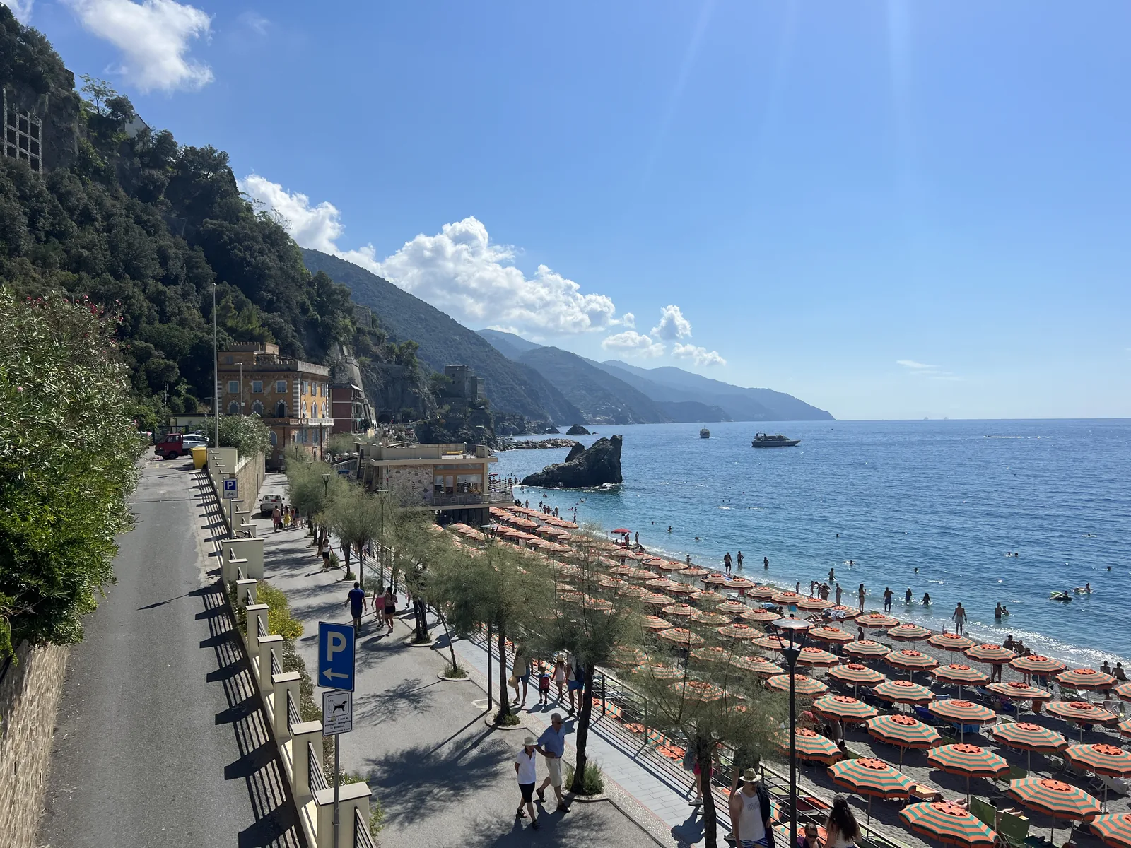 Promenade in Monterosso al Mare above the beach of Fegina with rows of parasols, the coast towards Punta Mesco behind