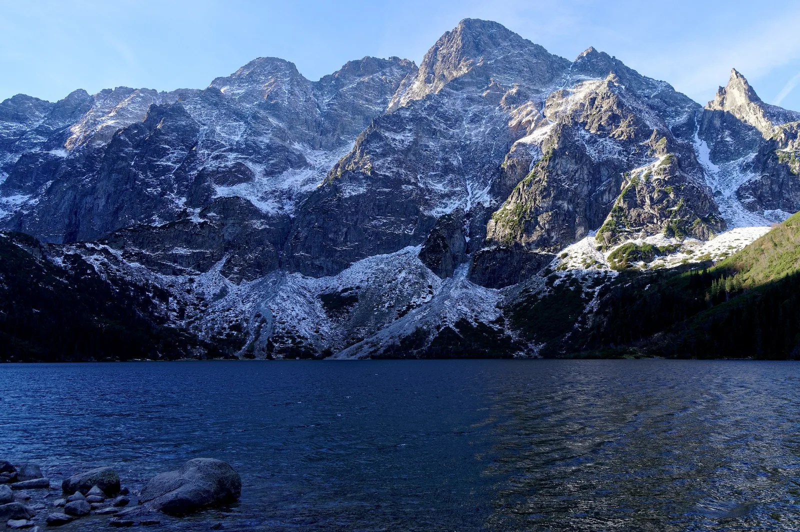 Morskie Oko in Tatra National Park in October, with the snow-covered Mięguszowieckie Szczyty behind and stones on the shore in the foreground