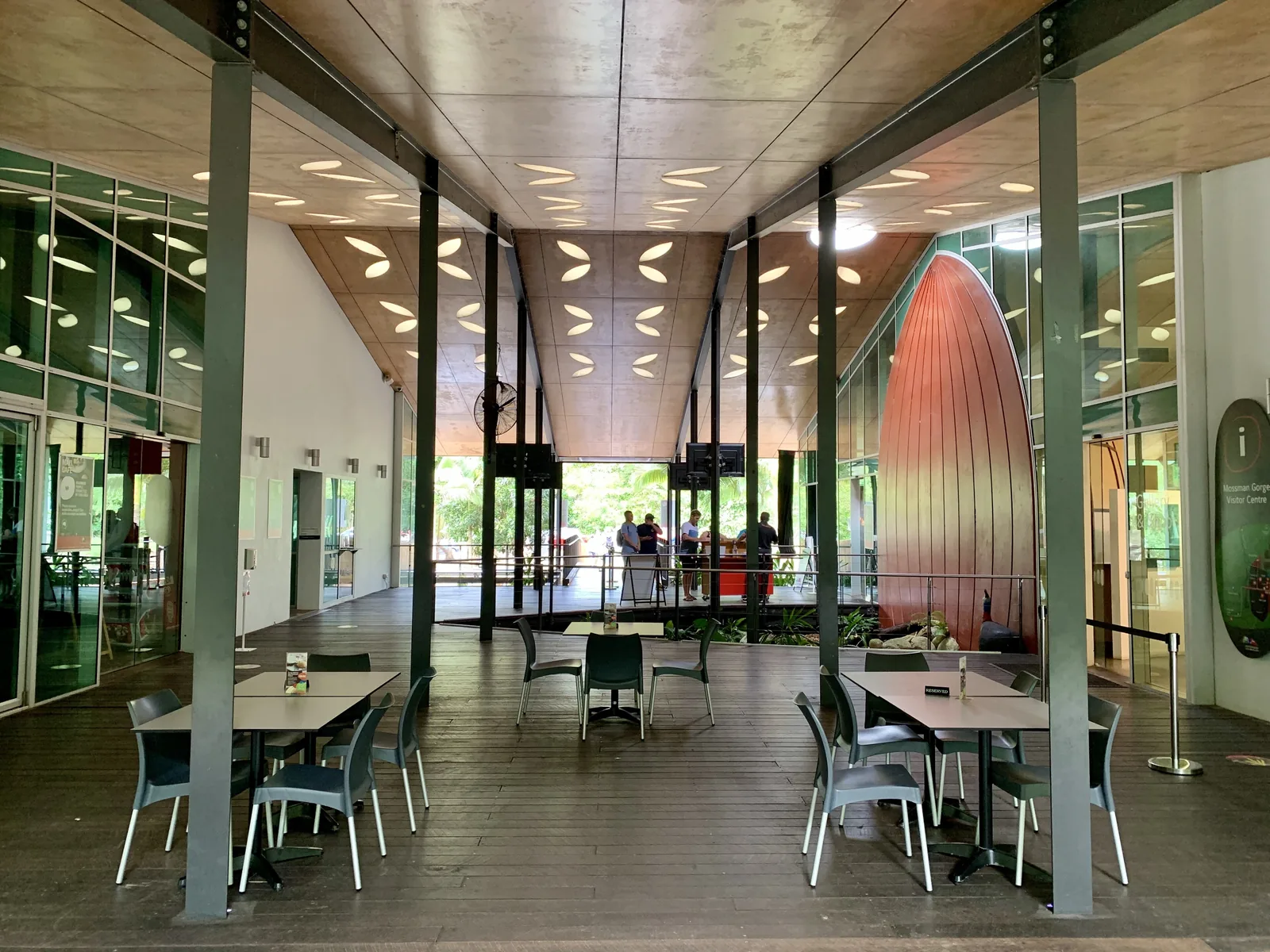 The open hall of the Mossman Gorge Centre with tables, glass walls and a tall copper-coloured sculpture
