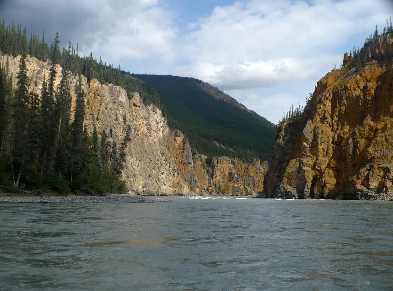 View from the water into Fourth Canyon in Nahanni National Park Reserve: high layered rock walls on both sides, the river flowing calmly between them
