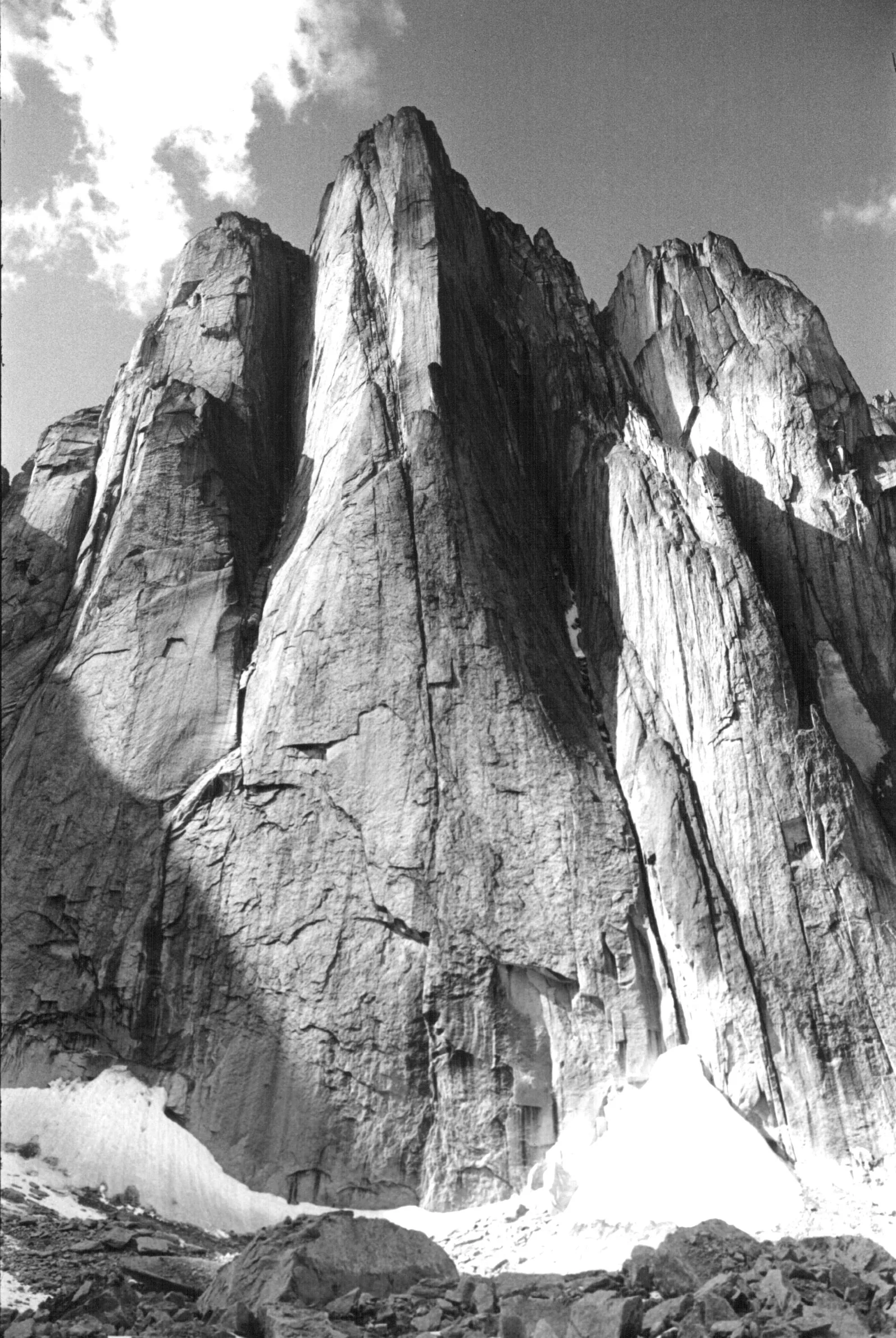 Black-and-white photo of the Lotus Flower Tower in Nahanni National Park Reserve: a huge vertical granite wall rises from a snowfield, with other rock towers beside it