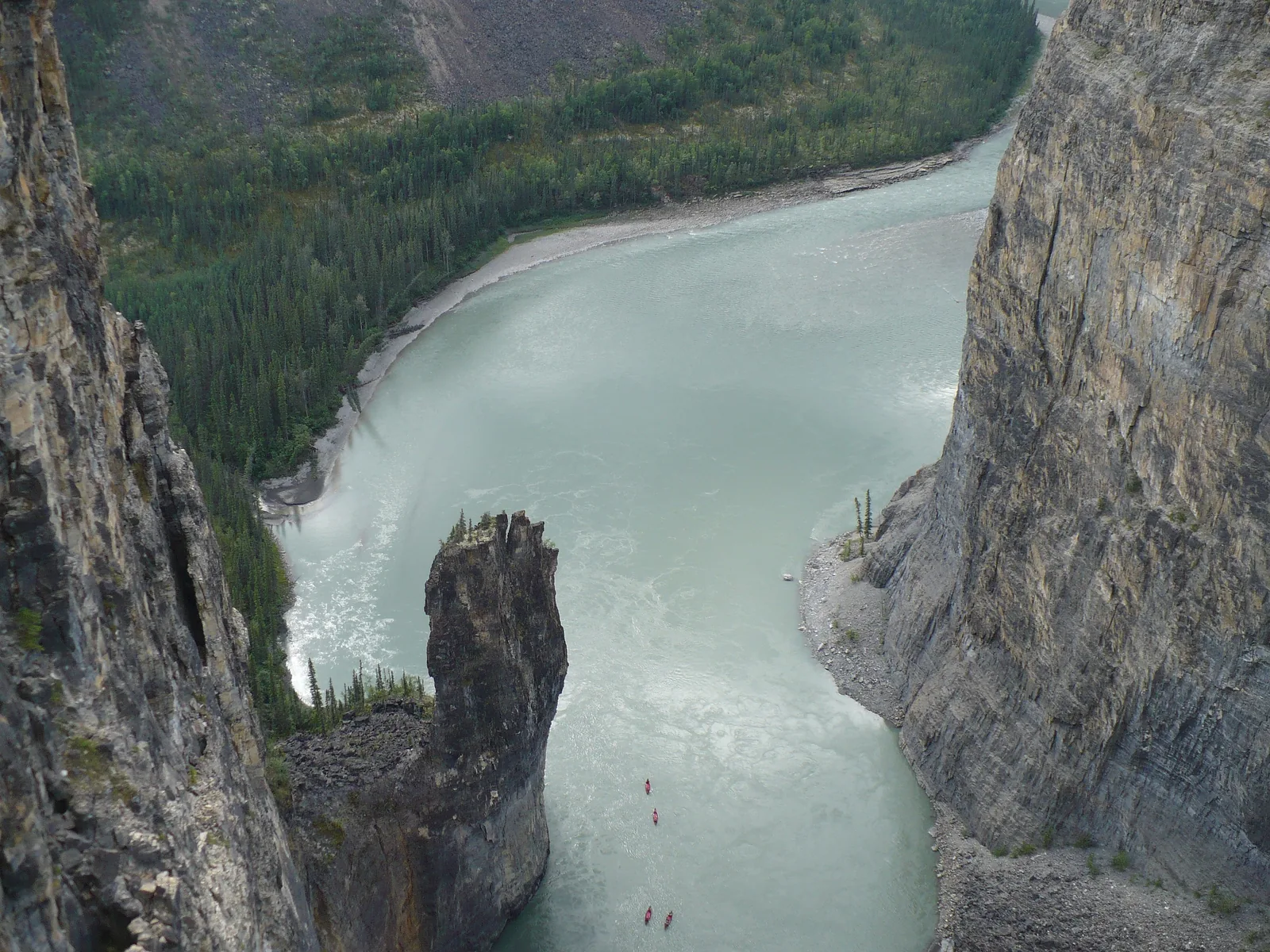 Aerial view of The Gate in Second Canyon of Nahanni National Park Reserve: the river makes a tight loop around a free-standing rock tower, tiny canoes visible on the water