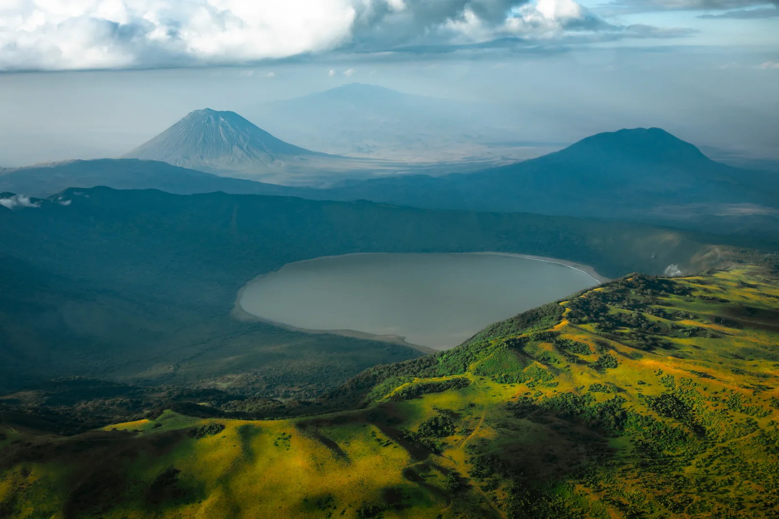 The crater lake of Empakaai between green walls, the cone of Ol Doinyo Lengai on the horizon