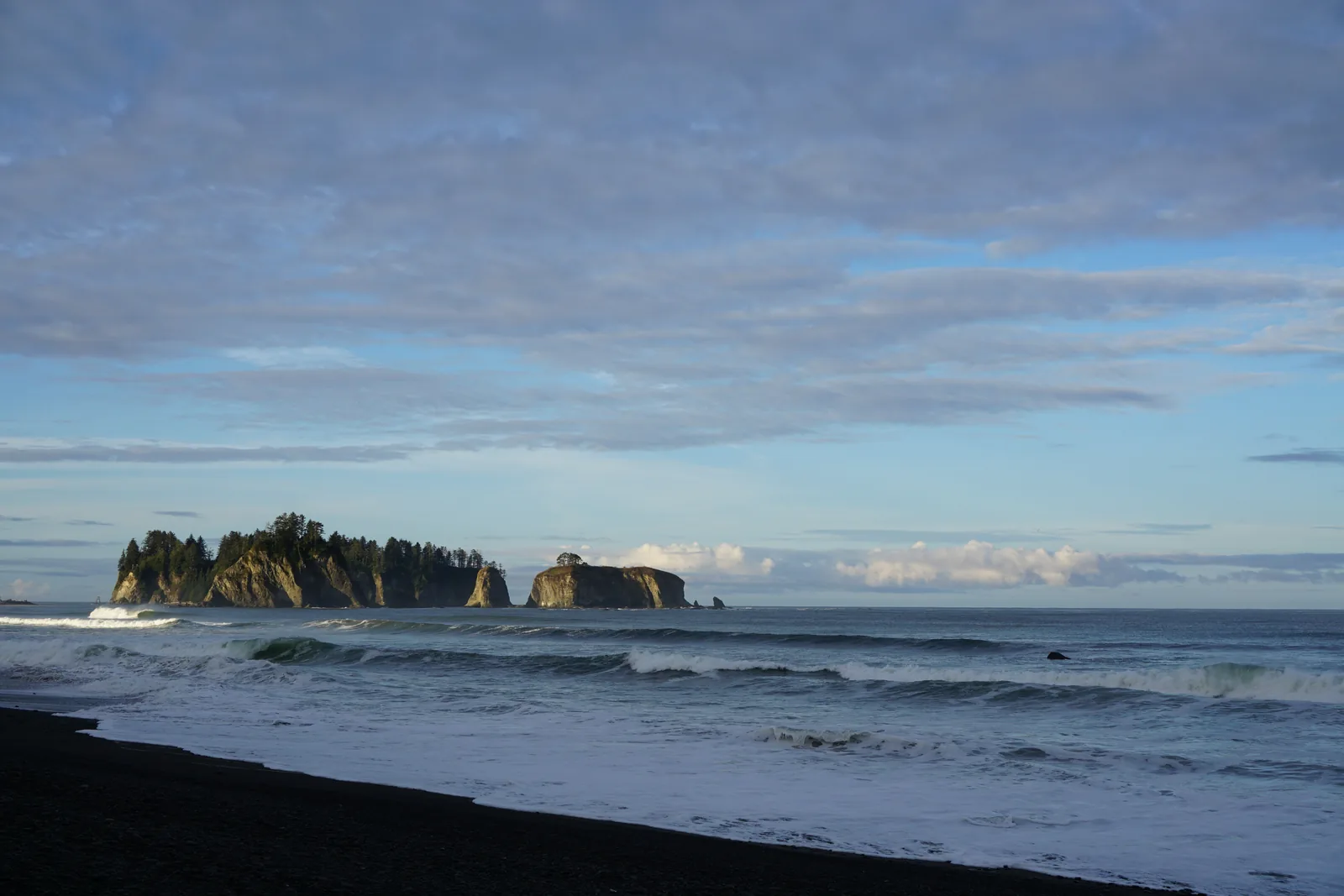 Rialto Beach in Olympic National Park in the morning: a dark pebble beach, surf and the forested rock island of James Island
