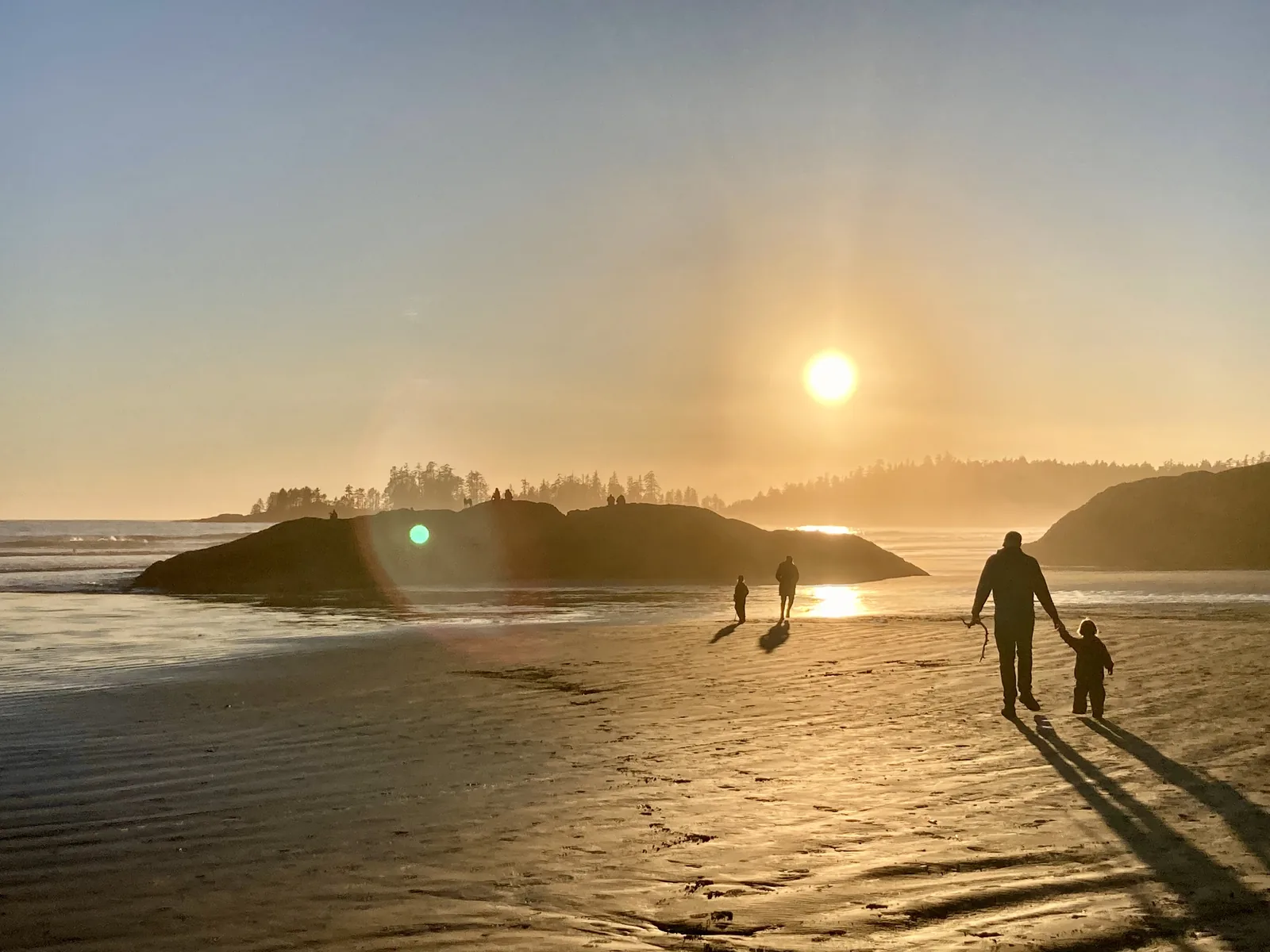 A family in silhouette on the wide sandy beach of Long Beach in Pacific Rim National Park Reserve, the low sun over the Pacific