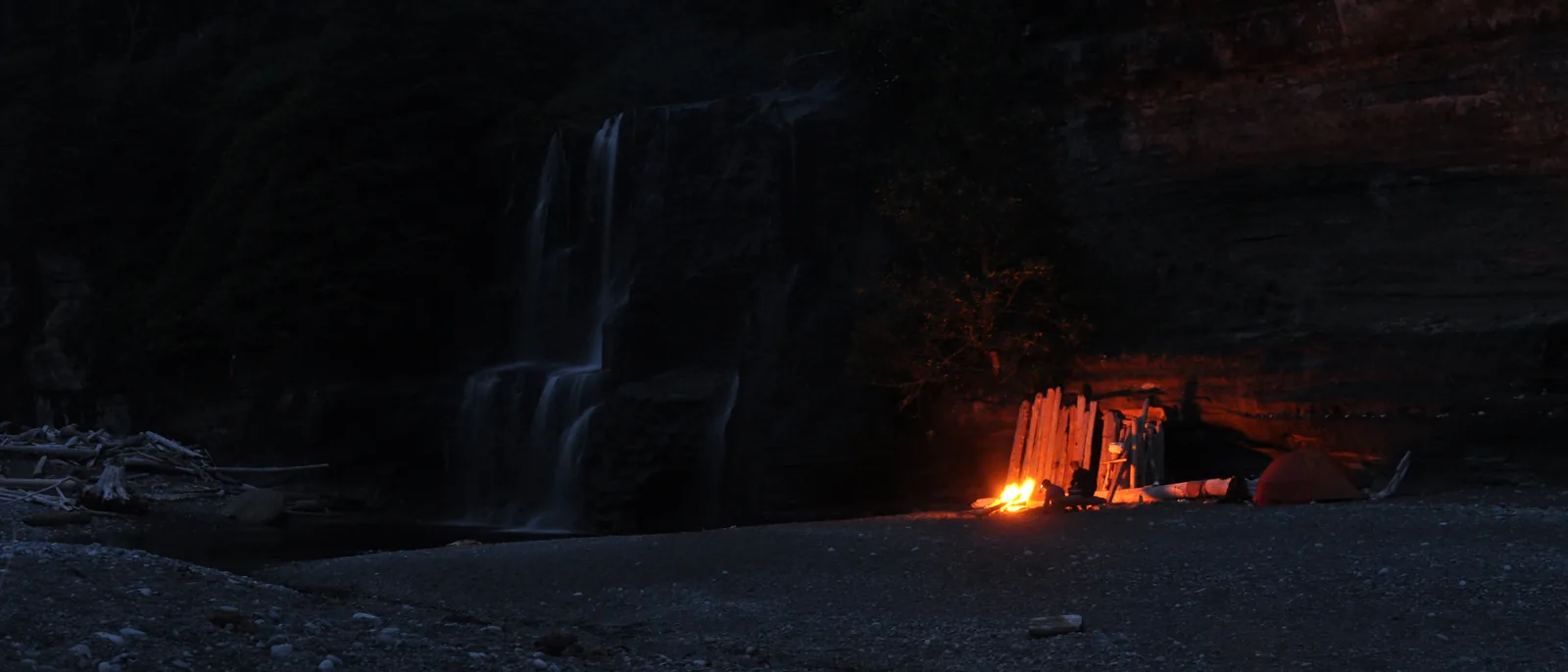 Night shot at the Tsusiat Falls campsite in Pacific Rim National Park Reserve: the waterfall on the left, the glow of a campfire under the rock overhang on the right