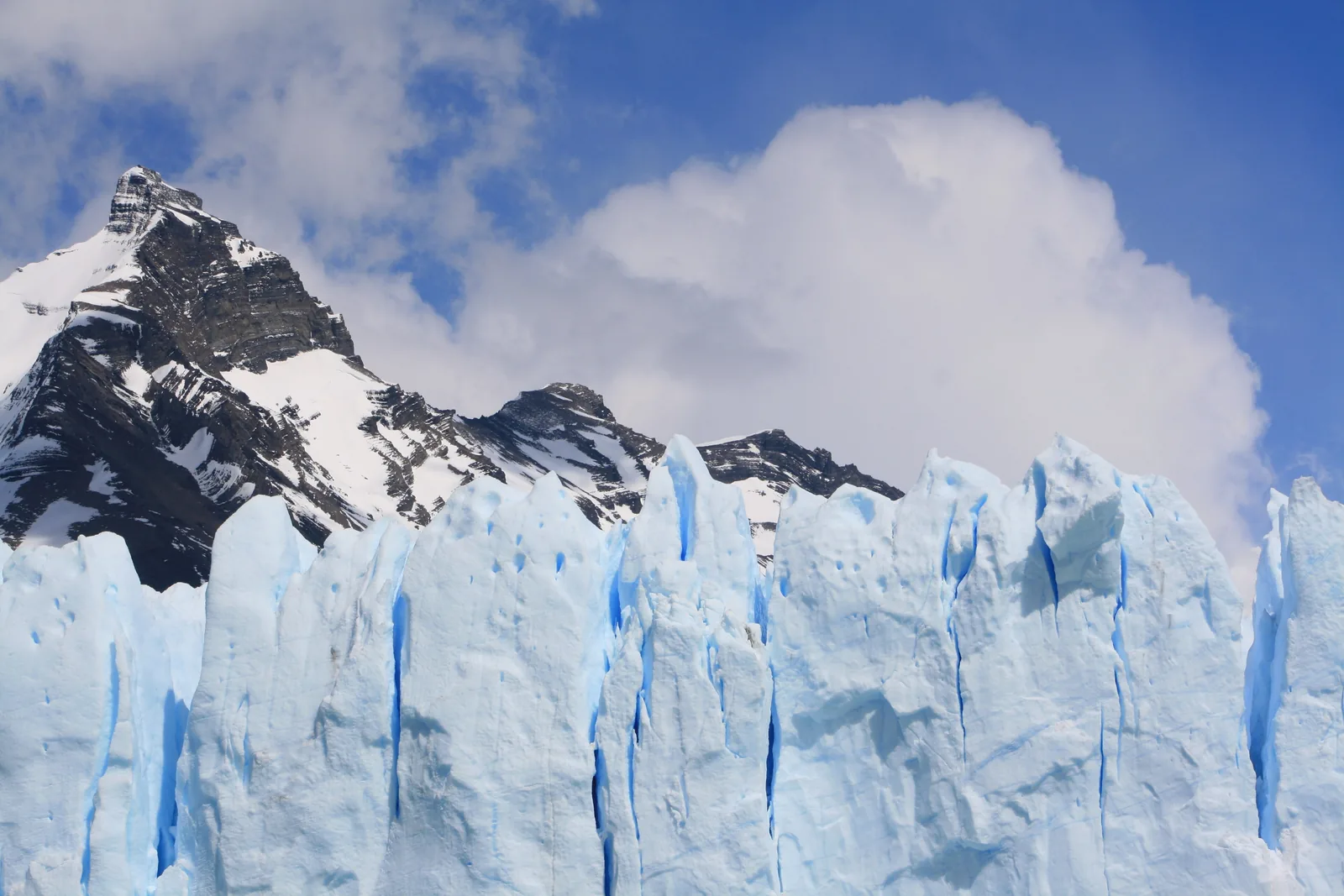 Tall blue-white ice towers at the front of the Perito Moreno Glacier in Los Glaciares National Park below a rugged, snowy peak
