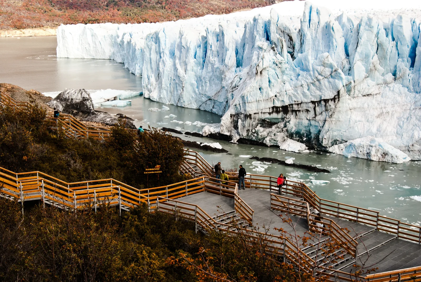 Visitors on the wooden walkways at the Perito Moreno Glacier in Los Glaciares National Park, the tall ice front and the lake behind