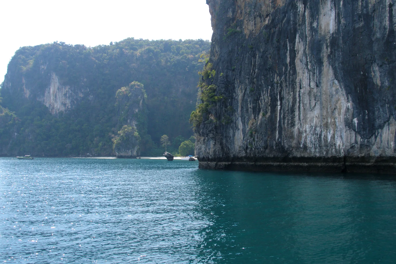 Dark green water in front of a sheer limestone wall at Ko Hong in Ao Phang Nga National Park, with more overgrown rocks behind