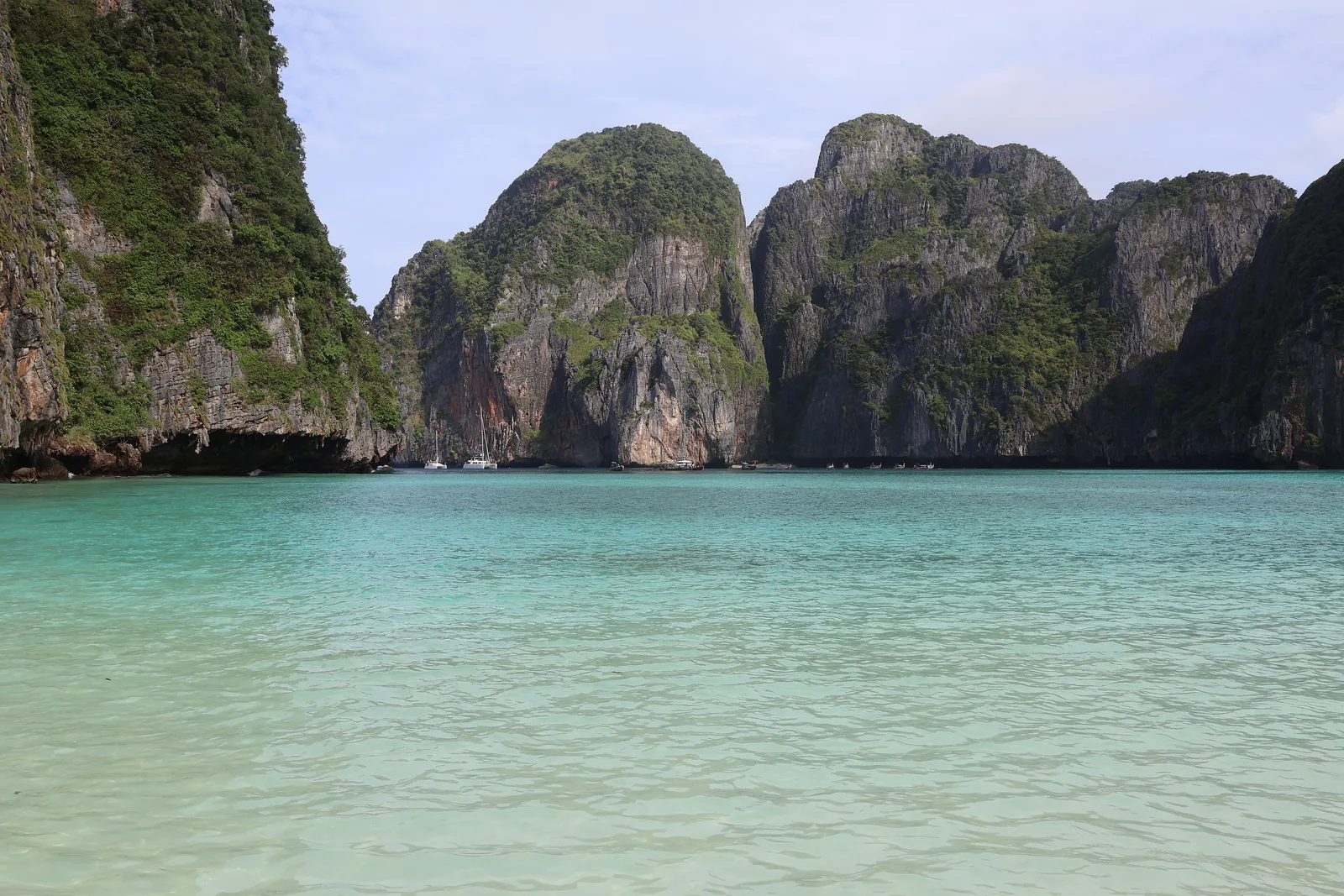 Shallow, pale green water in Maya Bay in Phi Phi National Park, with the dark limestone cliffs that enclose the bay behind