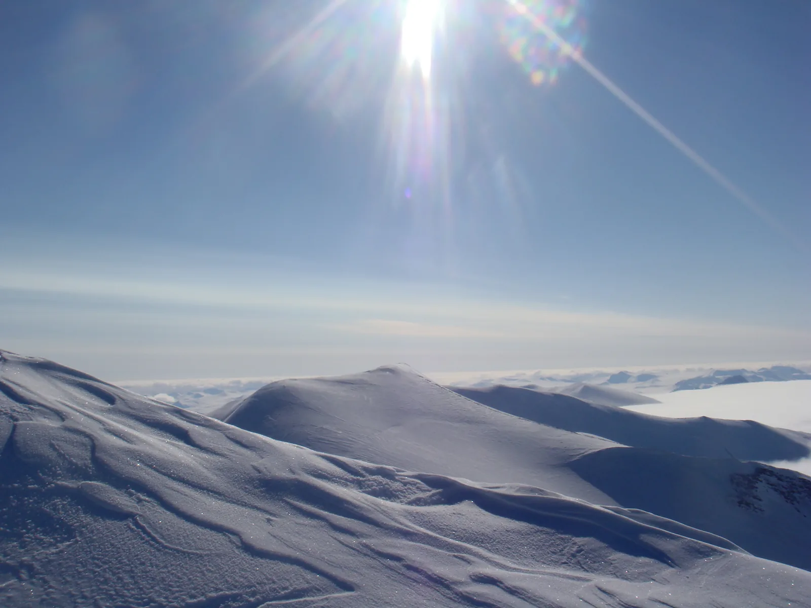 View from the summit in Quttinirpaaq National Park over wind-blown snow ridges to a vast icefield, the low sun in a blue sky above