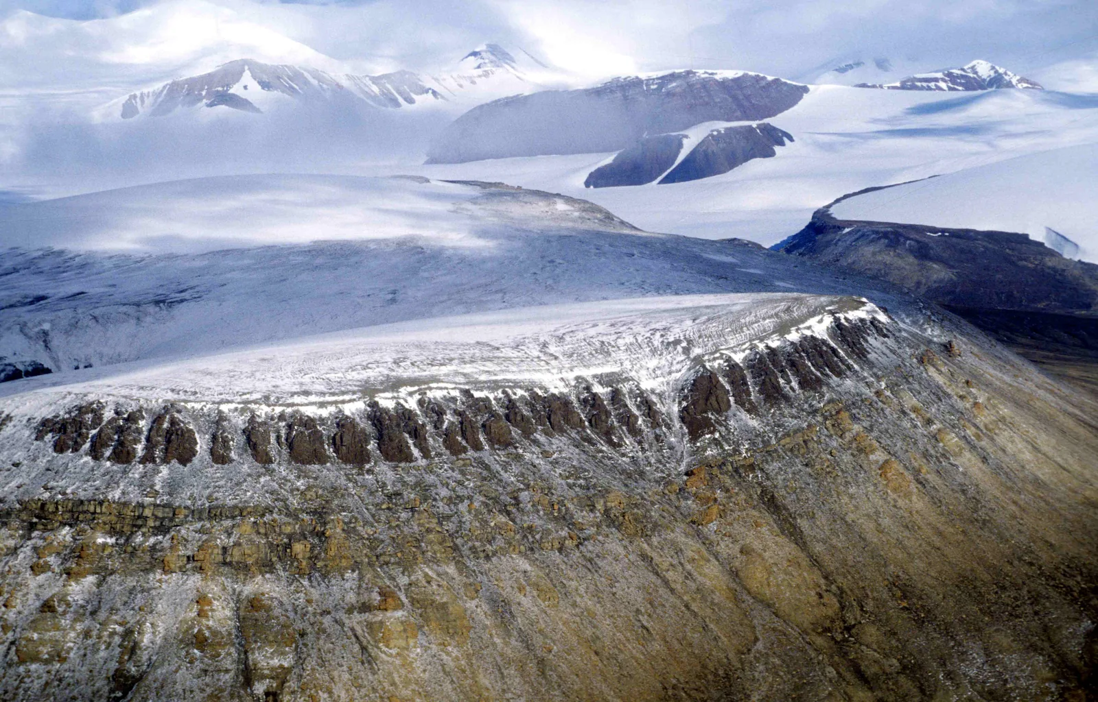Dark, ground-down ridges rise from a vast icefield in Quttinirpaaq National Park, an icy rock edge in the foreground