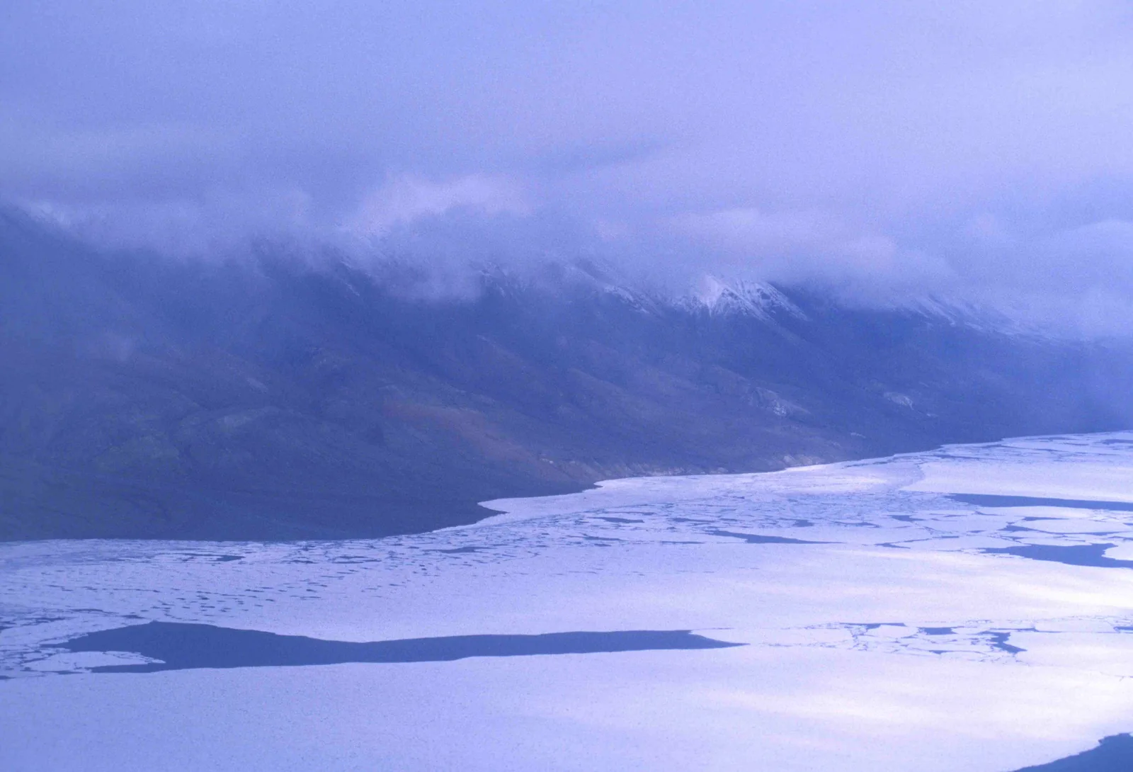 Frozen Lake Hazen in Quttinirpaaq National Park with broken ice floes, a long mountain range behind under low clouds