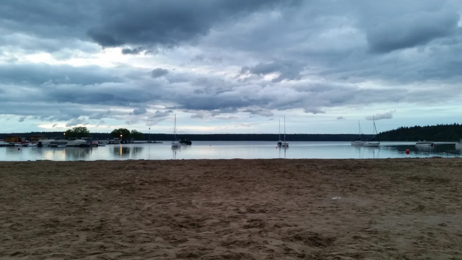 The main beach of Wasagaming on Clear Lake in Riding Mountain National Park, sailing boats by the water, the wide lake beyond under clouds