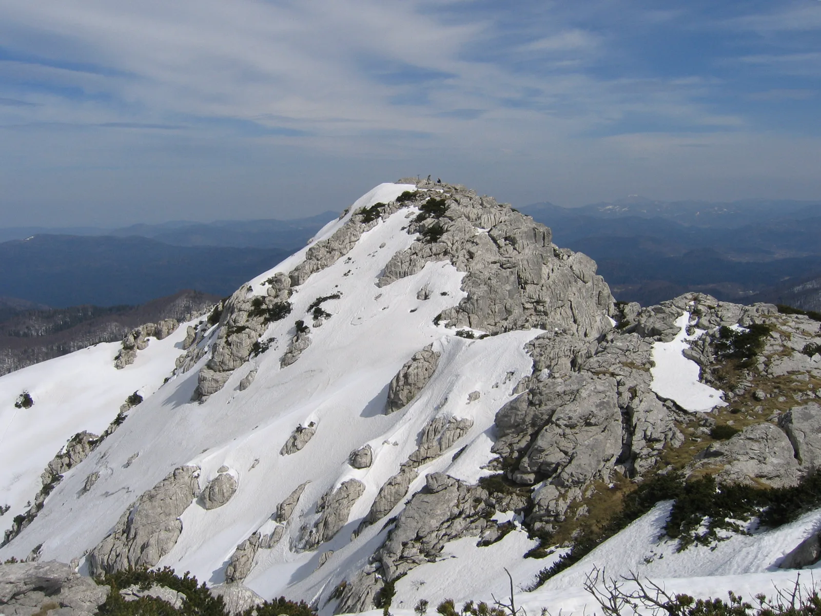 The snow-covered rocky summit of Risnjak in Risnjak National Park above wooded ridges