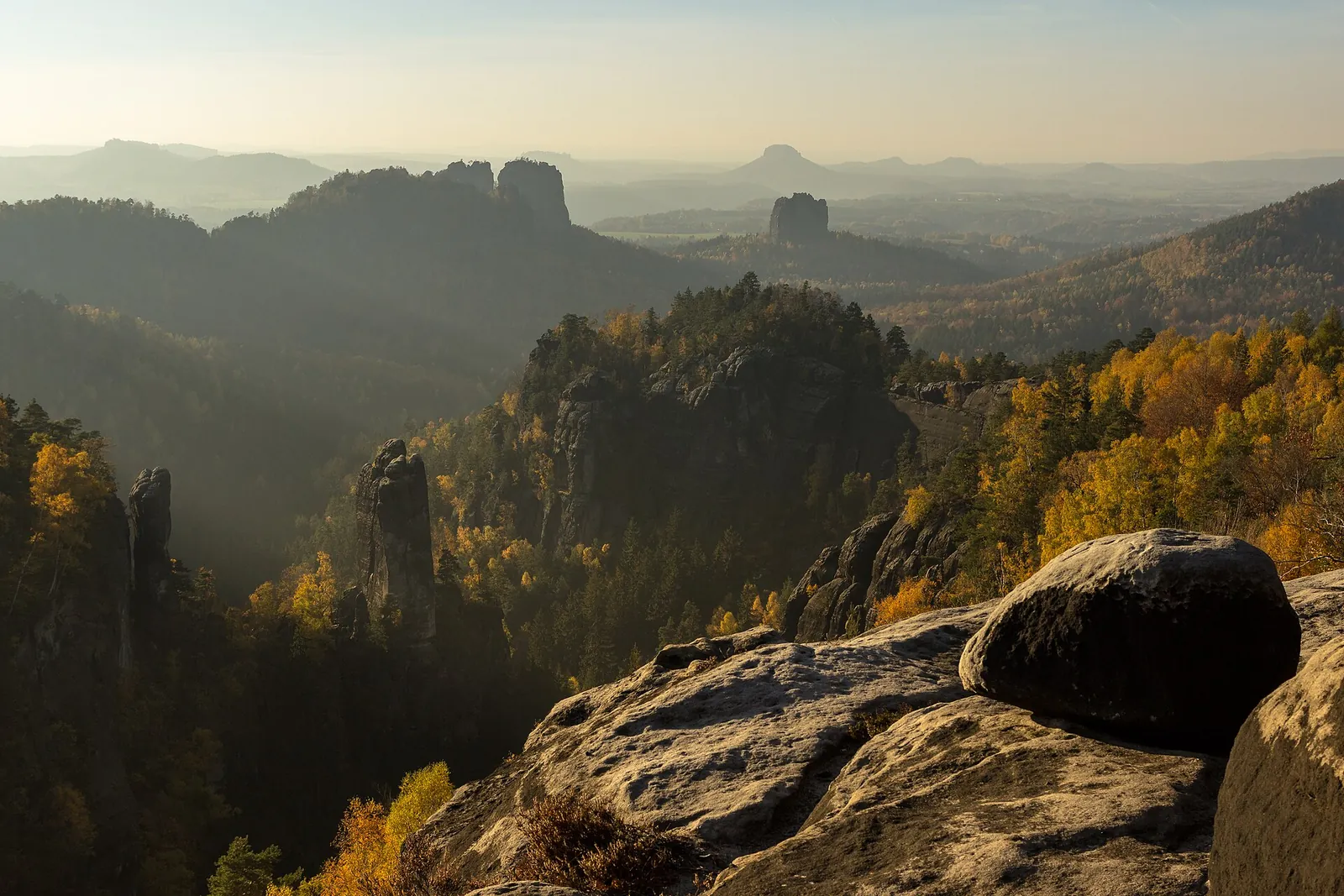 View from the Carolafelsen in Saxon Switzerland National Park westwards over rock towers and autumn-coloured forest against the light