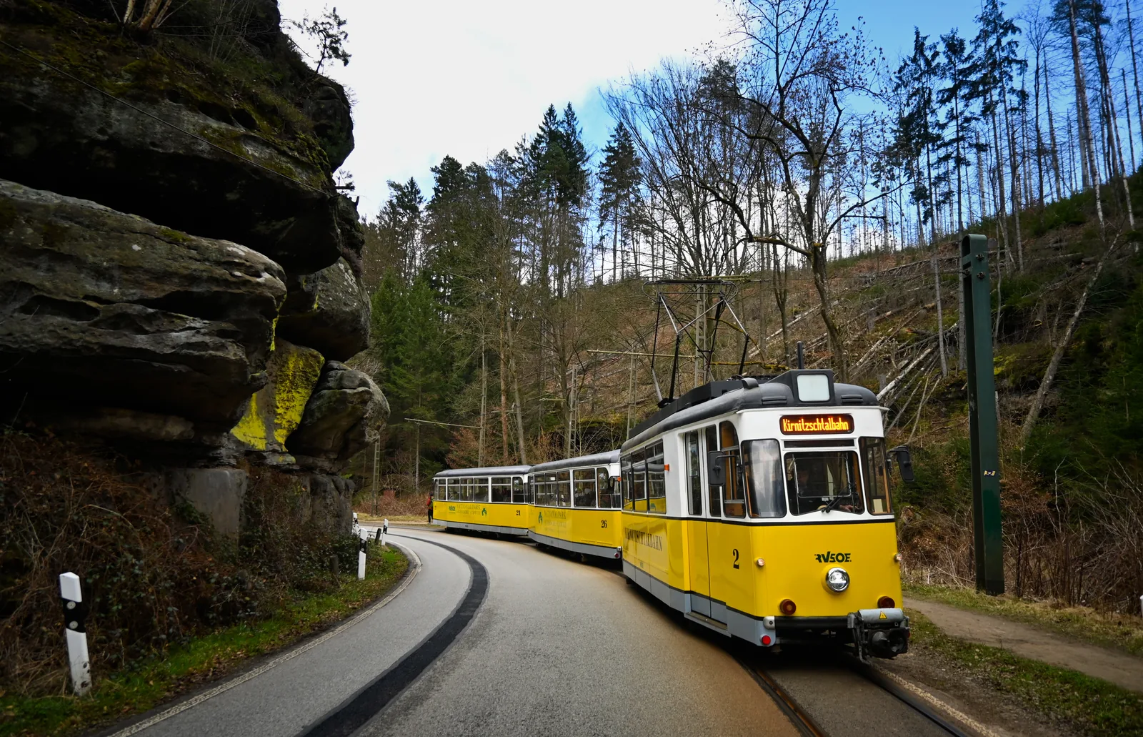 Yellow Kirnitzschtal tram running through the wooded Kirnitzschtal valley in Saxon Switzerland National Park, sandstone rocks at the roadside on the left