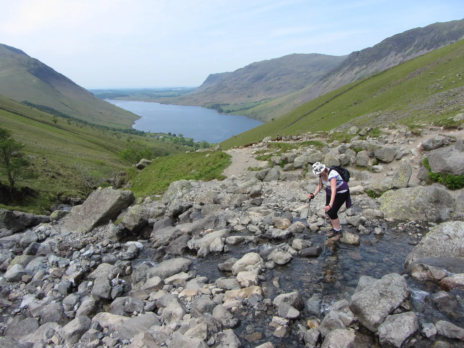 A walker crossing Lingmell Gill on the way to Scafell Pike, with Wast Water behind, in the Lake District National Park