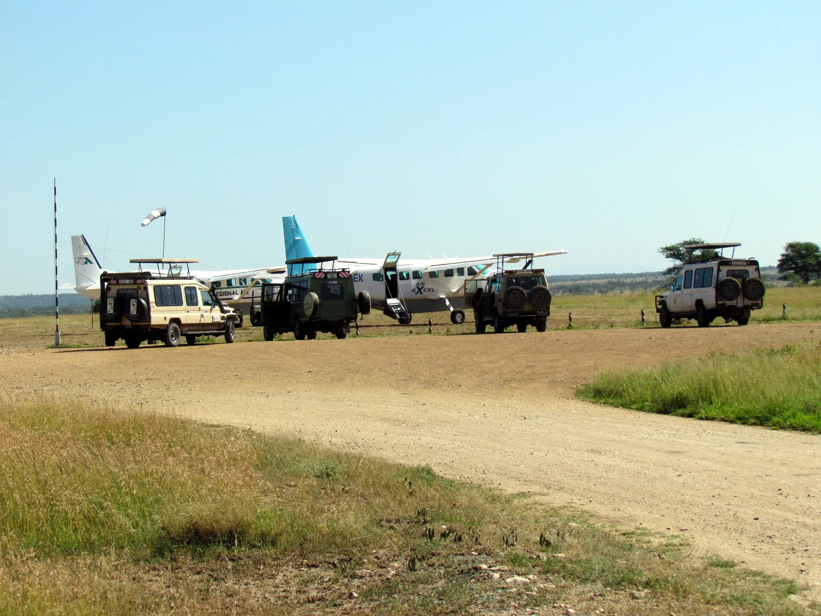 Safari vehicles wait next to a small aircraft at Seronera airstrip in Serengeti National Park, the gravel runway in the foreground