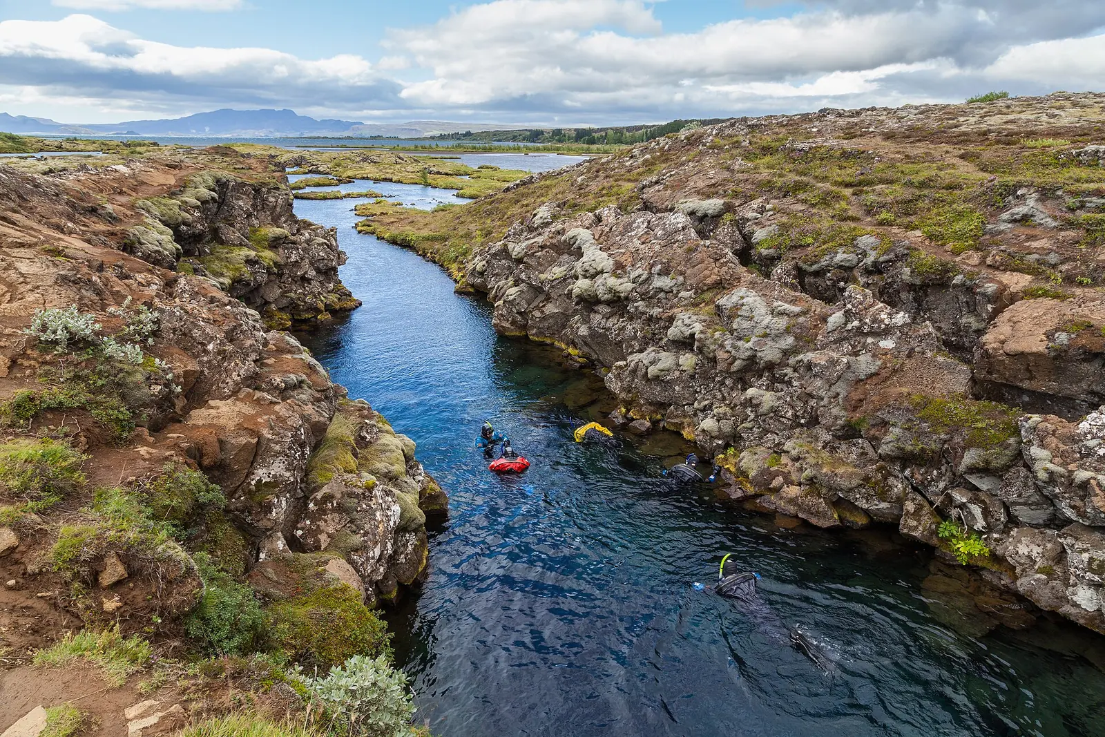 Snorkellers in the Silfra fissure in Þingvellir National Park drift through clear blue water between moss-covered lava rocks