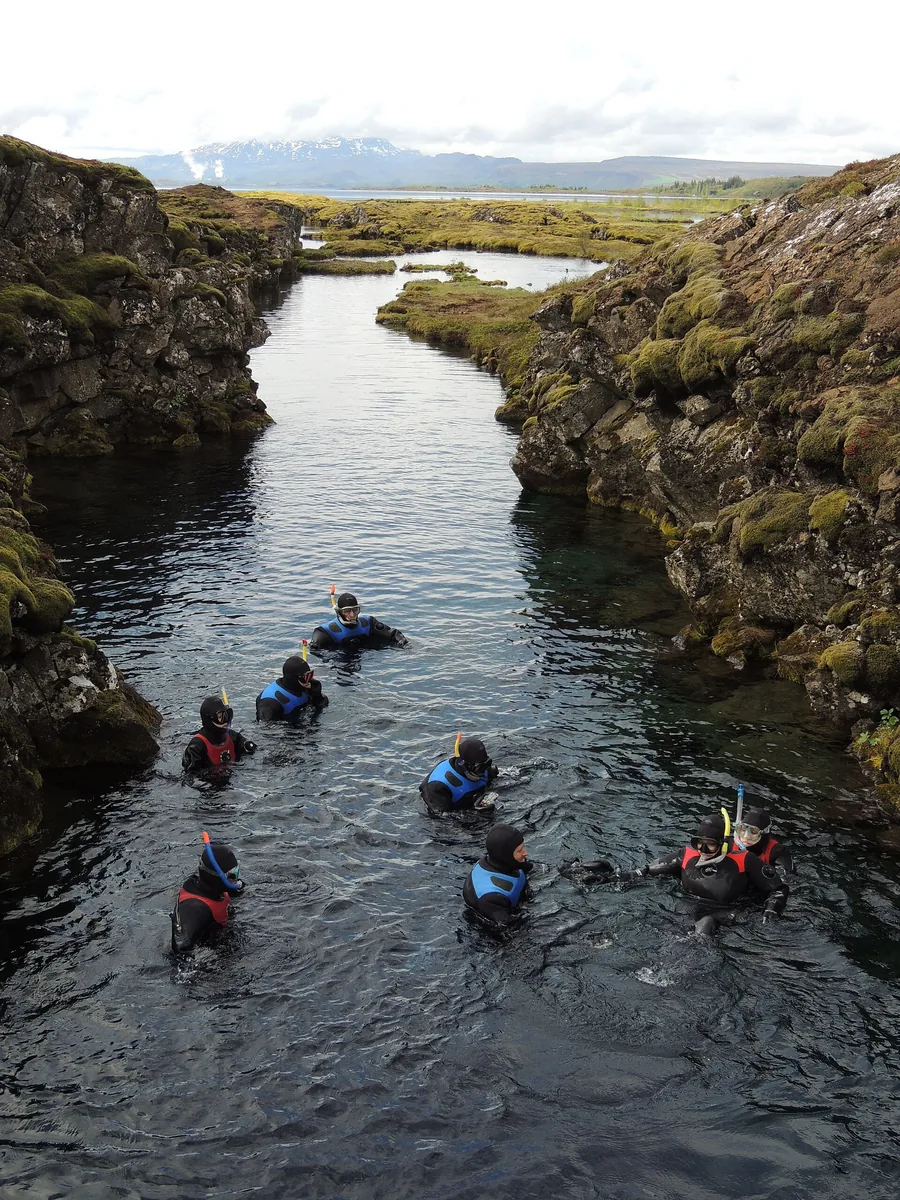 A group of snorkellers in the Silfra fissure, photographed from above, between dark rock walls