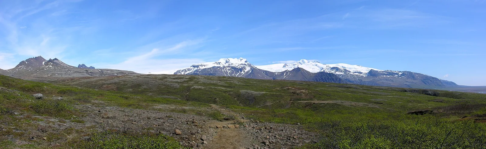 The trail to Svartifoss in Skaftafell runs over green slopes, Hafrafell and snowy peaks behind