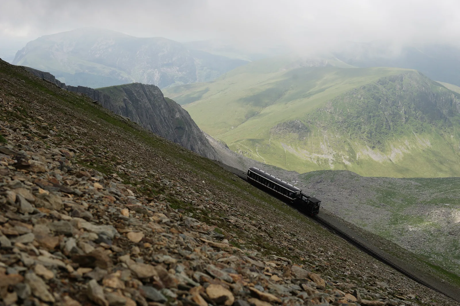 A Snowdon Mountain Railway train on the stony flank of Snowdon in Snowdonia National Park, valleys and cloud behind