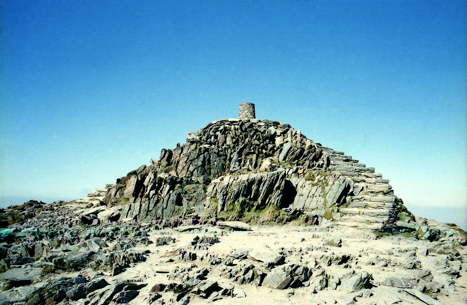 The rocky summit of Snowdon (Yr Wyddfa) in Snowdonia National Park with its stone plinth and steps under a blue sky