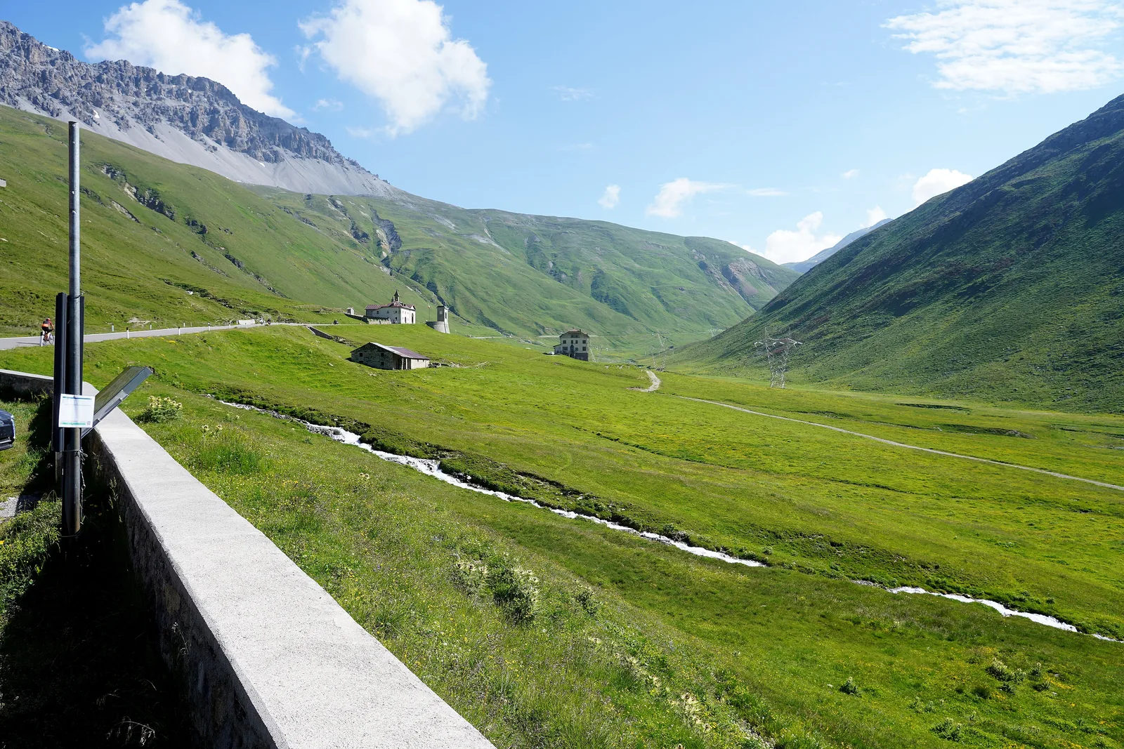 The green high valley Valle del Braulio in Stelvio National Park west of the summit, with a road wall and a stream