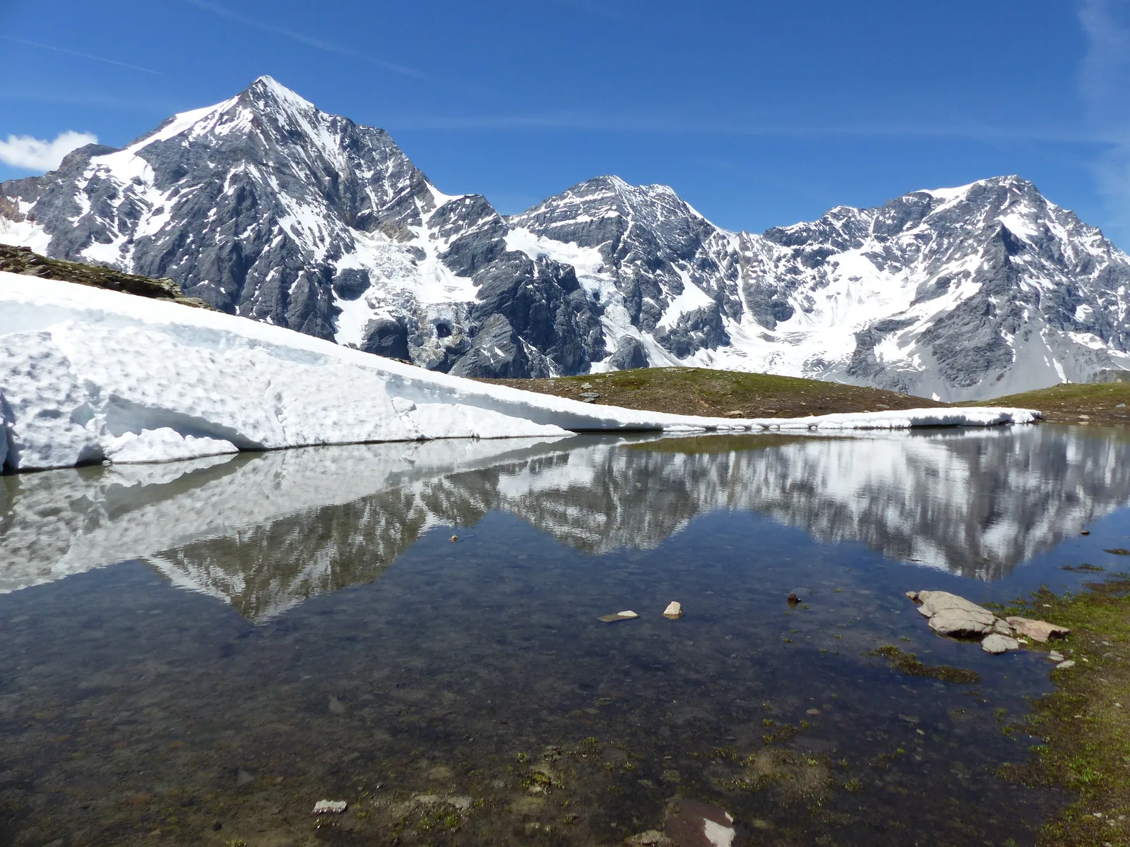 Gran Zebrù, Monte Zebrù and the Ortler in Stelvio National Park reflected in a small mountain lake with patches of snow